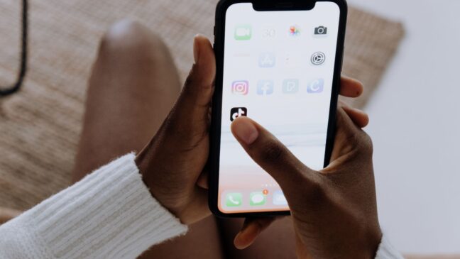 A person holding a phone in their hand, clicking on the TikTok app icon.